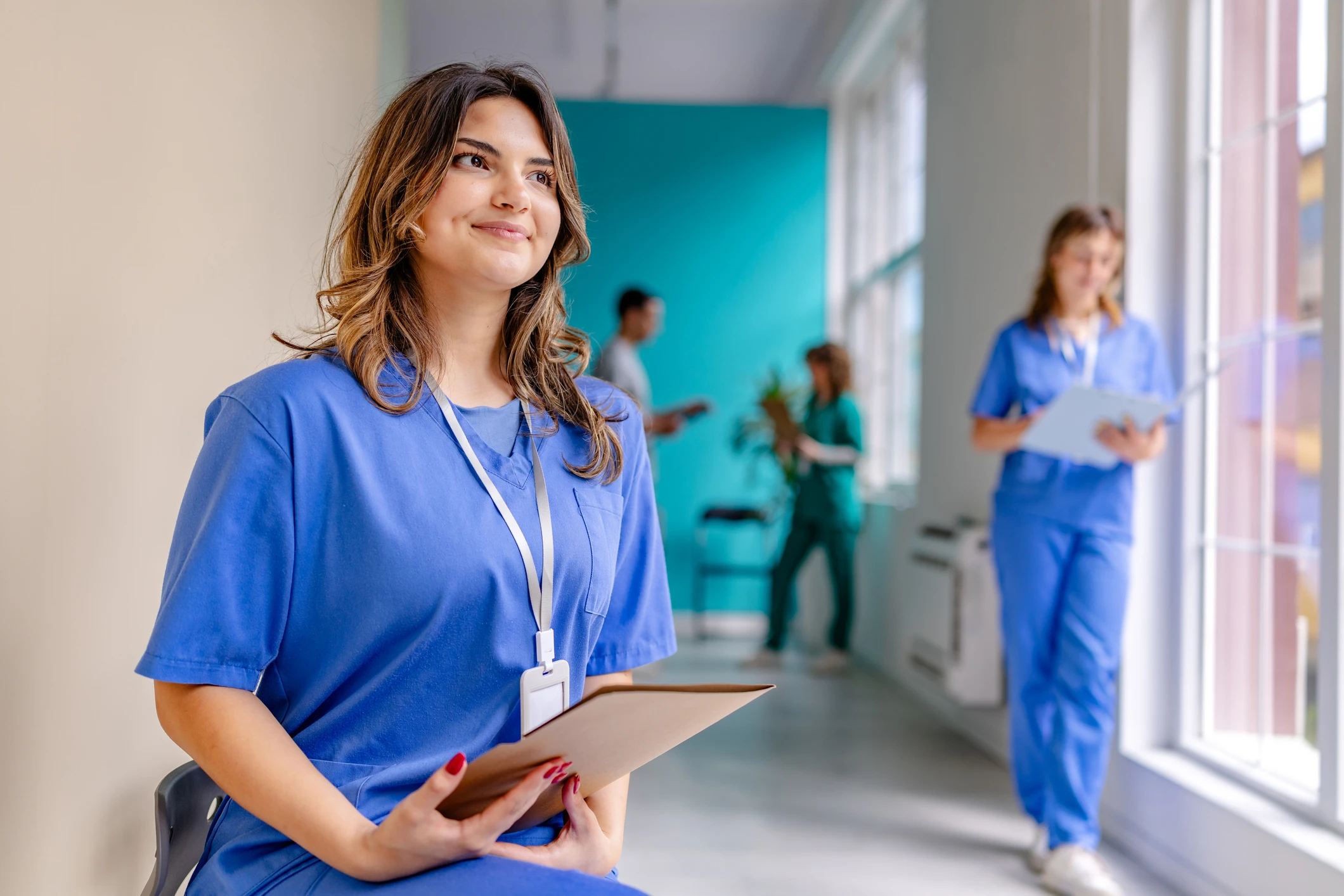 Smiling nurse with clipboard in hospital corridor.