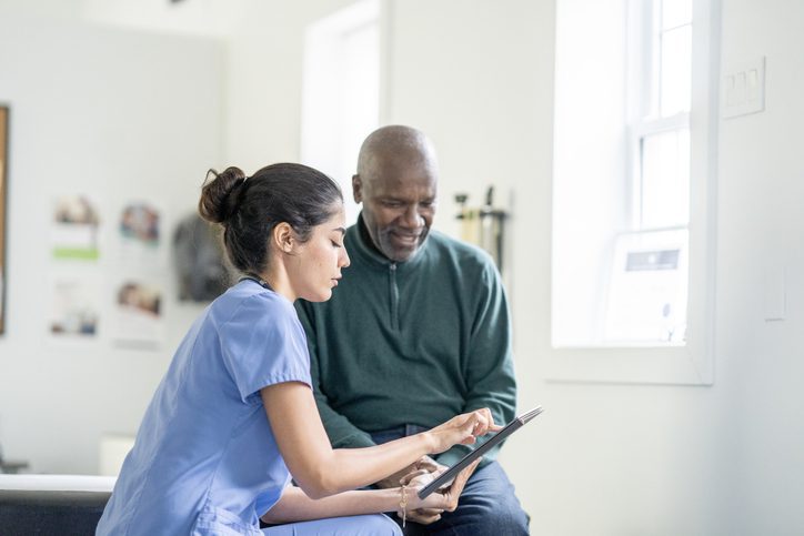 Nurse assisting elderly man with tablet.