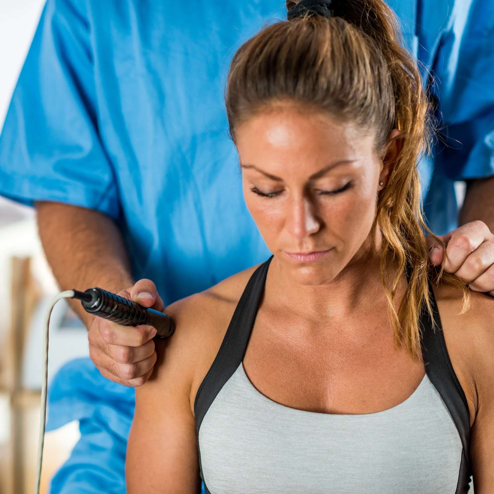 Physiotherapist treating woman's shoulder with device.
