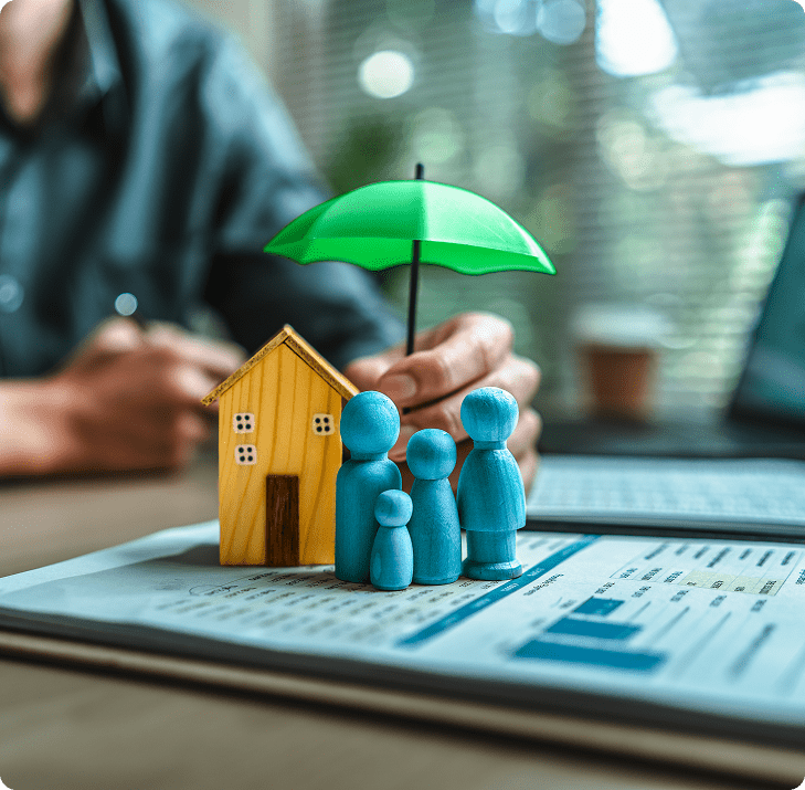 Family figurines under umbrella beside house model.